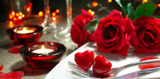 Festive table place setting for Valentines day dinner with red roses and burning candles