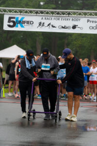 Massachusetts AdaptX Unified 5K 2025 inclusive road race two men helping third man pushing walker